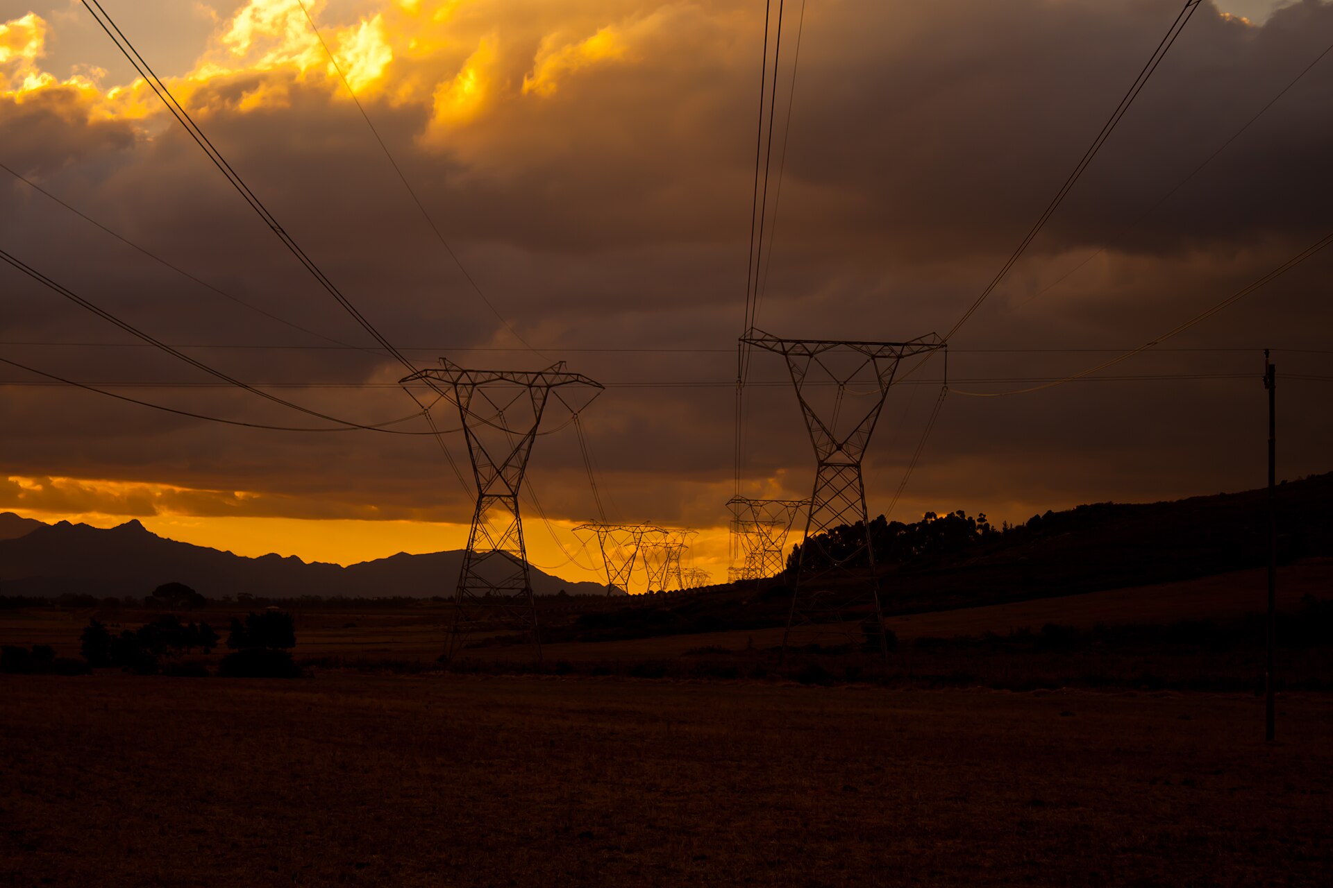 South African transmission network · Photo by Azwi, CC BY-SA 3.0, via Wikimedia Commons High-voltage transmission pylons at sunset on the South African grid